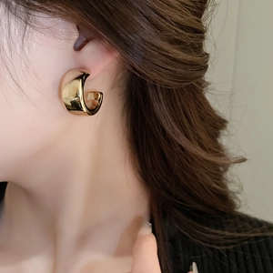 Gros plan d'un mannequin portant une boucle d'oreille en C en métal doré au fini poli