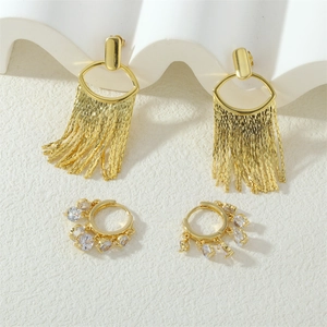 Detail of gold fringe earrings and zircon studs on a textured white background