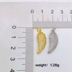 Gold and silver angel wing pendants with tiny crystals beside a measuring ruler