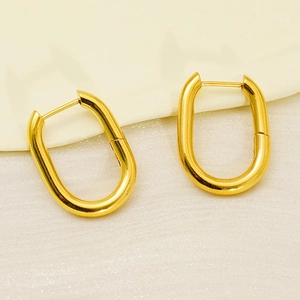 Detailed close-up of gold U-shaped oval earrings with smooth metallic finish on beige fabric
