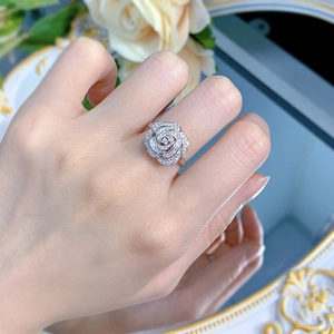 Macro shot of silver camellia ring with pavé-set crystals worn on finger near white roses