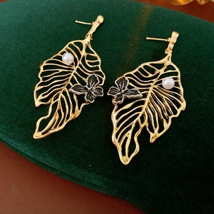 Detail view of golden leaf earrings with white pearls and black butterflies on velvet