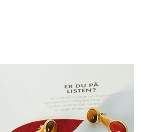 Detail of gold-plated stud earrings featuring oval amber and red gemstones on fabric