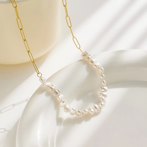Detail of baroque pearl necklace with gold paperclip chain on white ceramic plate