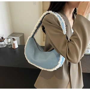 Détail d'un sac à bandoulière demi-lune en denim bleu clair avec franges sur un modèle