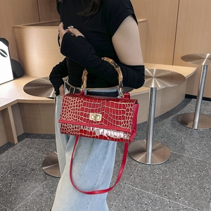 Detail of red crocodile texture handbag featuring a natural bamboo handle and gold lock