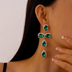 Close-up of elegant green teardrop gemstone earrings with diamond pavé and tassels