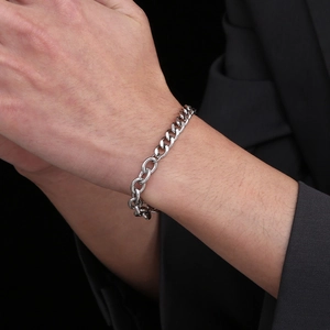 Détail d'un bracelet gourmette en acier titane avec fermoir OT porté avec un costume noir