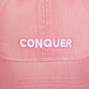 Macro shot of embroidered CONQUER text and cotton twill texture on pink baseball cap