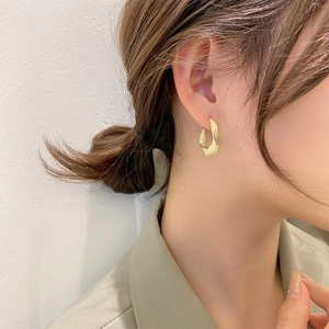 Close-up of elegant gold twisted hoop earring worn by a model in a minimalist style