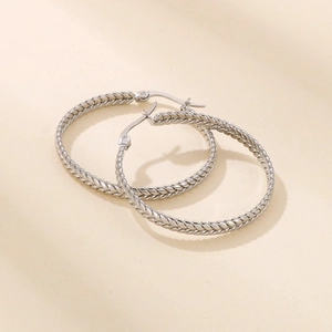 Close-up of silver geometric hoop earrings with intricate braided wheat pattern texture