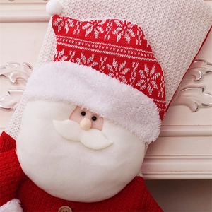 Close-up of a knitted red Christmas stocking featuring a 3D Santa Claus face by a fireplace
