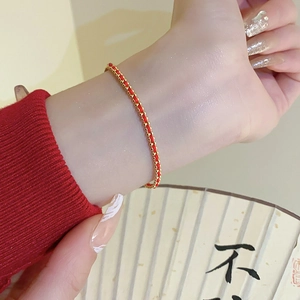 Detail of hand-woven red rope bracelet with gold beads against a traditional fan background