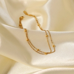 Detail of elegant 18K gold-plated double-layer bead chain bracelet on silk fabric