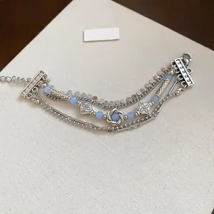 Detail of silver layered bracelet with light blue beads and floral charms on cream base
