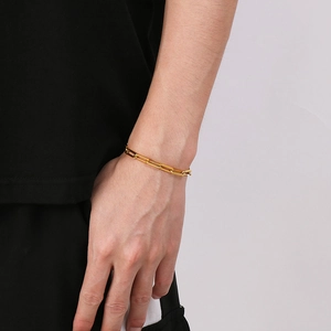 Detailed view of a gold-colored metal chain link bracelet worn by a male model