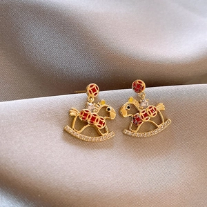 Golden rocking horse earrings with red patterns and pearls on grey silk background