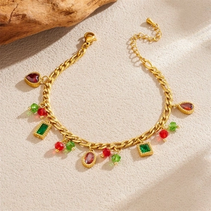 Close-up of gold chain bracelet with red and green gemstones on a natural stone background