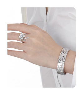 Detail of silver S925 textured flower ring and wide metal cuff bracelet on model hand