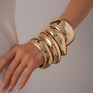 Close-up of polished gold-plated chunky metal bangles layered on a model's wrist
