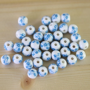 Macro shot of blue and white floral ceramic beads scattered on light wood for DIY jewelry