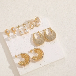 Detailed collection of 14K gold plated pearl and zircon earrings on white stone surface
