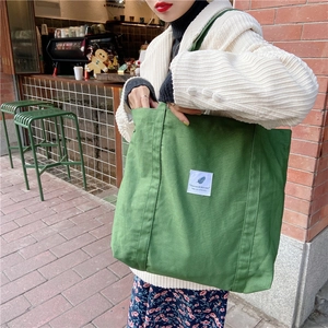Dettaglio borsa tote in tela verde con toppa bianca e tracolla larga in stile minimal