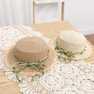 Dettaglio ravvicinato di due cappelli in paglia di rafia con decoro a nastro di foglie