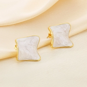 Macro detail of irregular gold-plated earrings with white marble-patterned enamel finish