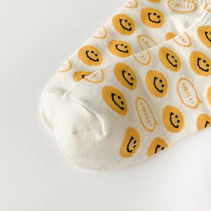 Close-up of white cotton knitted sock showing the toe stitching and yellow smile face icon