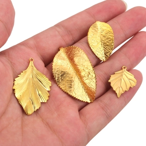 Golden stainless steel leaf pendants in various shapes shown on palm for scale