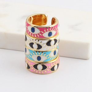 Close-up of four colorful enamel evil eye open rings stacked on white marble surface