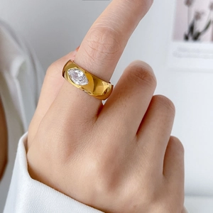 Detail shot of a wide gold-plated steel ring featuring a marquise-cut zircon on a finger