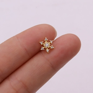 Close-up of a gold snowflake stud earring with tiny clear zircons on a soft pink backdrop