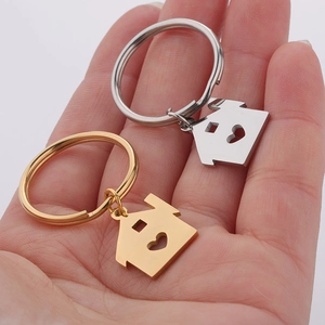 Detail showing gold and silver house-shaped keychains with heart cutouts held in hand