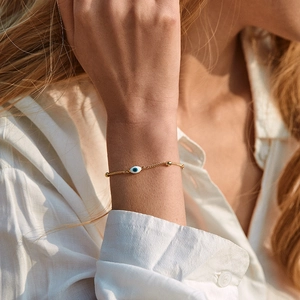 Detailed view of an 18K gold-plated Evil Eye bracelet worn on a wrist in natural light