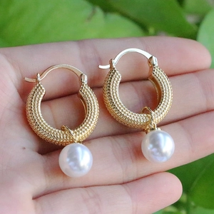Detailed close-up of U-shaped gold textured earrings with elegant round white pearls