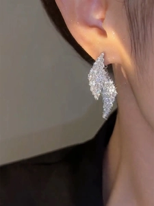 Close-up of sparkling leaf-shaped silver earrings with micro-set stones on a model