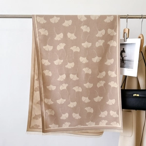 Detail of beige cashmere-feel scarf with white ginkgo leaf pattern and fine fringe trim