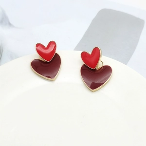 Close-up of double-layered red enamel heart stud earrings on white ceramic tray