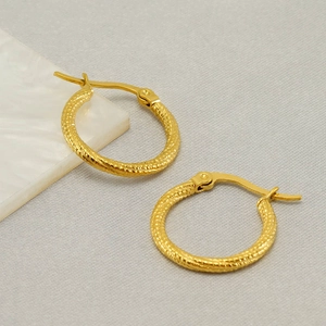 Golden stainless steel hoop earrings with textured spiral design on marble surface