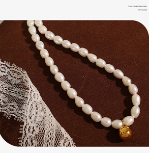 Detail of freshwater pearl necklace with gold ball pendant on brown background