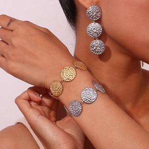 Dettaglio di bracciali e orecchini con dischi martellati oro e argento su una modella