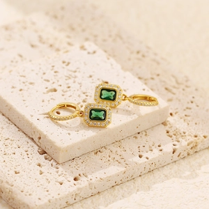 Macro shot of gold emerald earrings with micro-pave diamonds on beige travertine stone