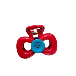 Minimalist red bow hair claw clip with blue button detail on a clean white background
