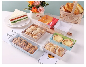 Various disposable sandwich boxes with clear lids and colorful paper bases on white table