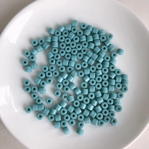 Macro view of cylindrical light blue acrylic tube beads in a white ceramic dish