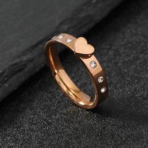 Rose gold stainless steel heart ring with sparkling rhinestones on textured stone background