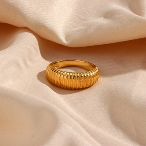 Close-up of golden vertical striped stainless steel ring on soft beige fabric
