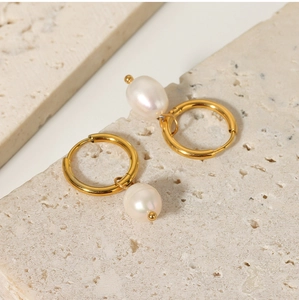 Detail view of gold titanium hoop earrings with white freshwater pearl drops on stone